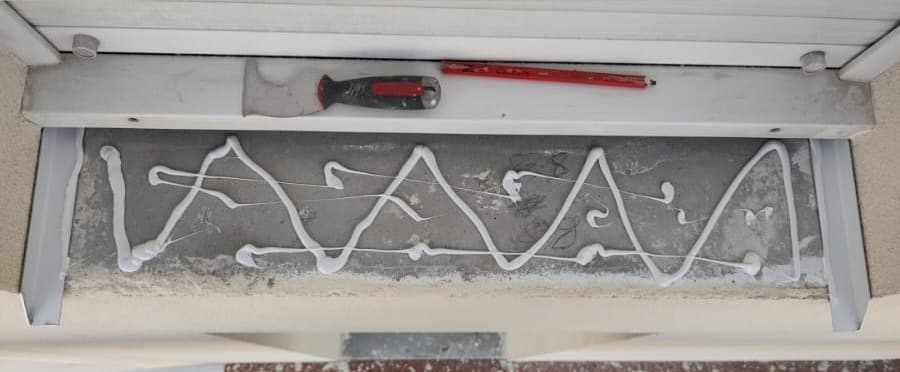 Cordon de colle appliqué en serpentin sur toute la longueur de l'appui de fenêtre, avant pose de la pièce en aluminium